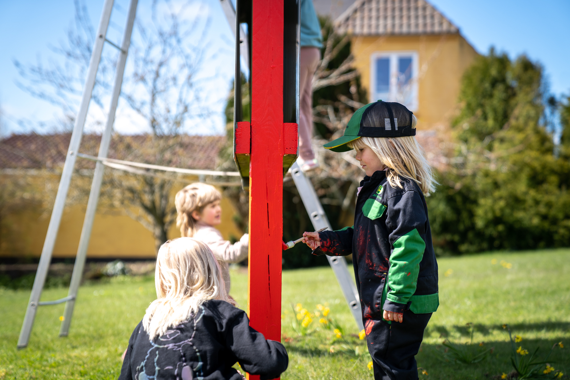 Forælder og børn maler skiltet ved hovedvejen på Boddum-Ydby Friskole og Børnehus, der er en projektbaseret friskole med børnehus i Sydthy - kom forbi til en rundvisning